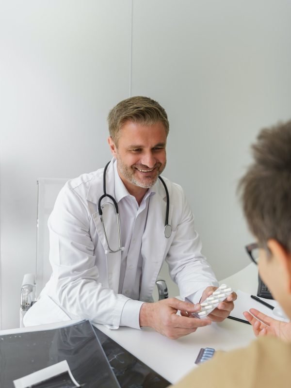 Close up of smiling doctor prescribing pills to female patient during appointment in his office